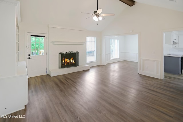 unfurnished living room with a fireplace, dark wood-style floors, wainscoting, beam ceiling, and ceiling fan