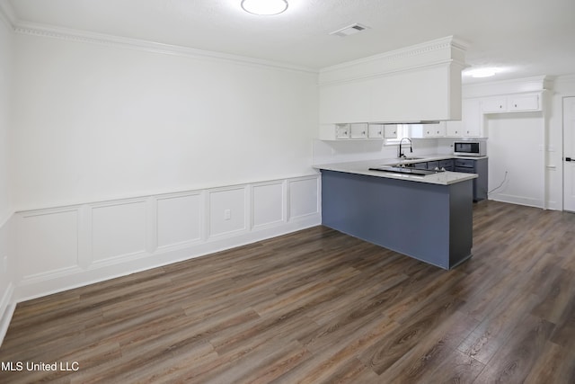 kitchen with white cabinets, a peninsula, dark wood finished floors, crown molding, and stainless steel microwave