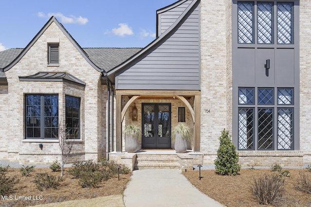 view of exterior entry with brick siding, french doors, metal roof, and a standing seam roof