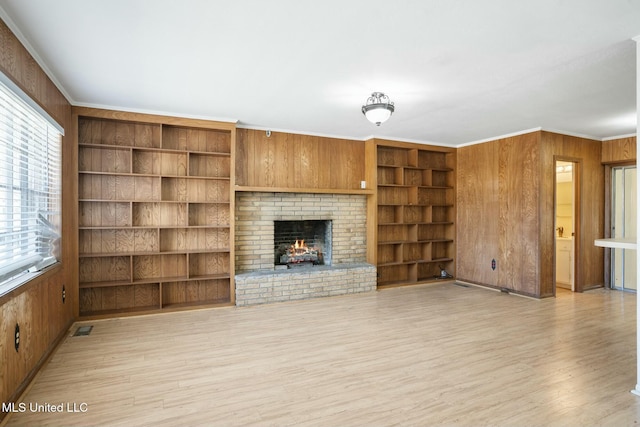 unfurnished living room featuring light wood-type flooring, wood walls, a fireplace, and crown molding