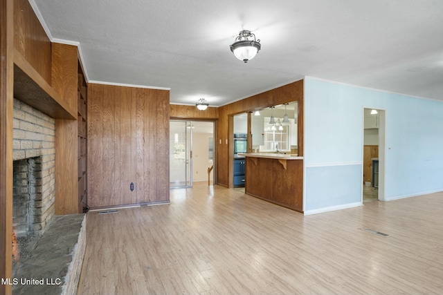 unfurnished living room with a brick fireplace, light wood-style flooring, visible vents, and ornamental molding