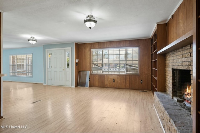 unfurnished living room featuring ornamental molding, light wood finished floors, wood walls, and a fireplace