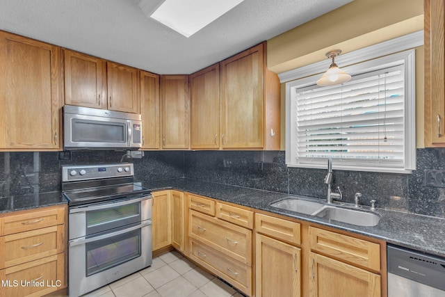 kitchen with light tile patterned floors, dark stone counters, a sink, decorative backsplash, and appliances with stainless steel finishes