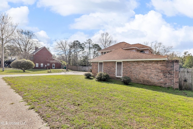 view of side of home with brick siding, a shingled roof, a lawn, and fence