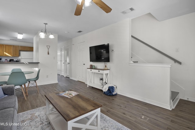 living room featuring ceiling fan with notable chandelier and dark wood-type flooring