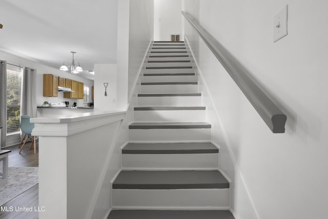 stairs featuring an inviting chandelier and wood-type flooring