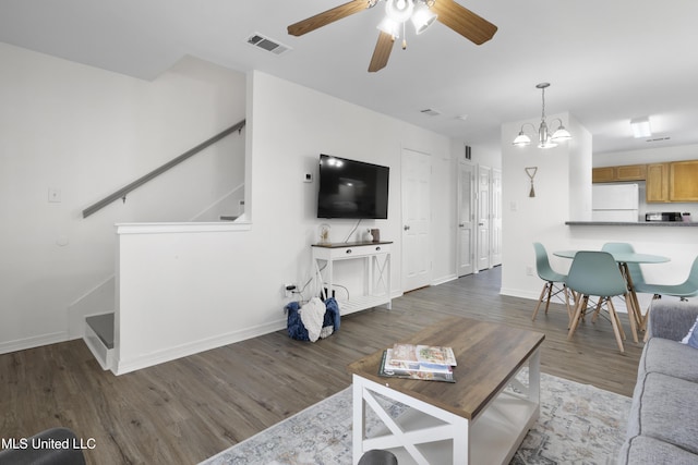 living room with ceiling fan with notable chandelier and dark wood-type flooring