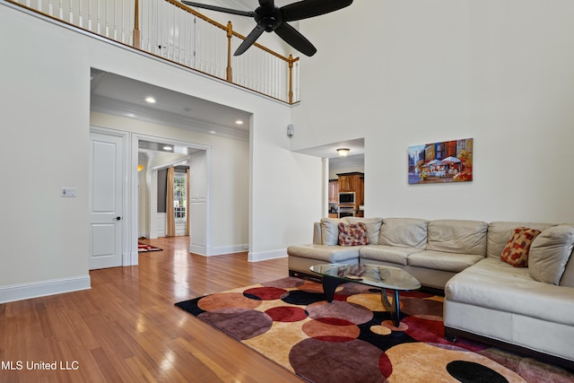 living room featuring hardwood / wood-style flooring, ceiling fan, crown molding, and a high ceiling