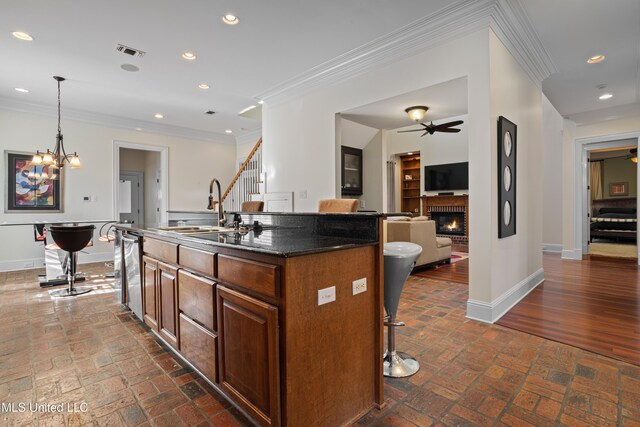 kitchen with a kitchen breakfast bar, sink, a brick fireplace, an island with sink, and decorative light fixtures