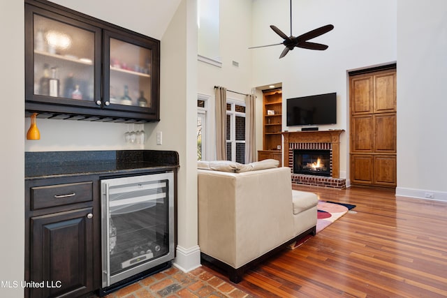 living room with indoor bar, a brick fireplace, ceiling fan, a towering ceiling, and beverage cooler