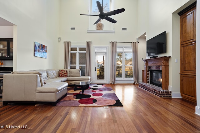 living room with dark hardwood / wood-style floors, ceiling fan, a high ceiling, and a brick fireplace