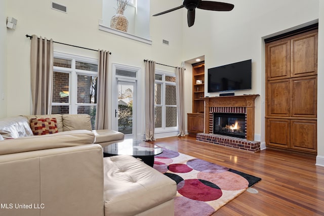 living room featuring ceiling fan, dark hardwood / wood-style flooring, a high ceiling, and a brick fireplace