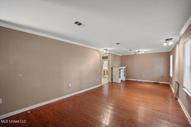 empty room featuring wood finished floors, visible vents, baseboards, and ornamental molding