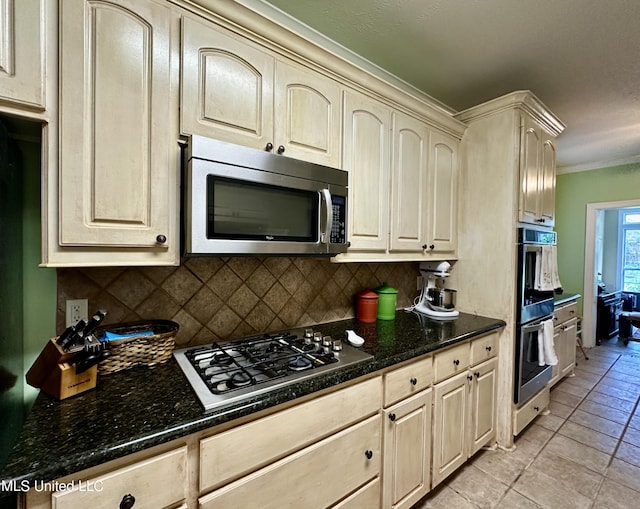 kitchen with crown molding, decorative backsplash, light tile patterned flooring, cream cabinetry, and stainless steel appliances