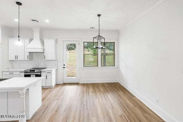 kitchen with stainless steel range with electric stovetop, pendant lighting, backsplash, premium range hood, and white cabinets