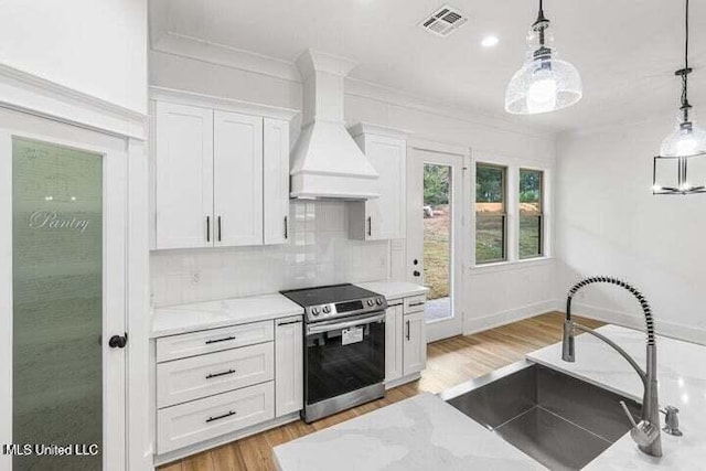 kitchen featuring custom exhaust hood, sink, hanging light fixtures, stainless steel electric range oven, and white cabinetry