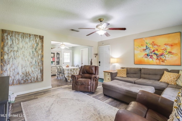 living room featuring wood finished floors, a textured ceiling, visible vents, ceiling fan, and baseboards