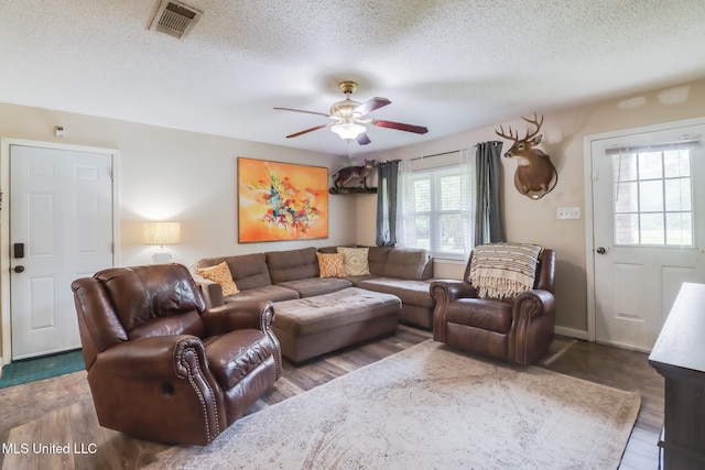 living area with a ceiling fan, visible vents, a textured ceiling, and wood finished floors