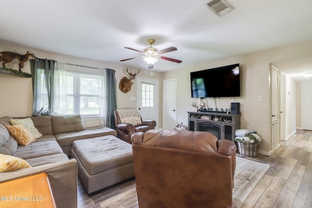 living room with ceiling fan, baseboards, visible vents, and light wood-style floors