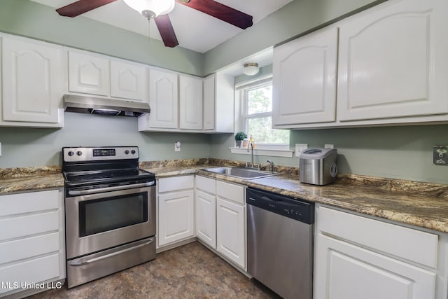 kitchen with stone finish floor, under cabinet range hood, a sink, white cabinetry, and appliances with stainless steel finishes