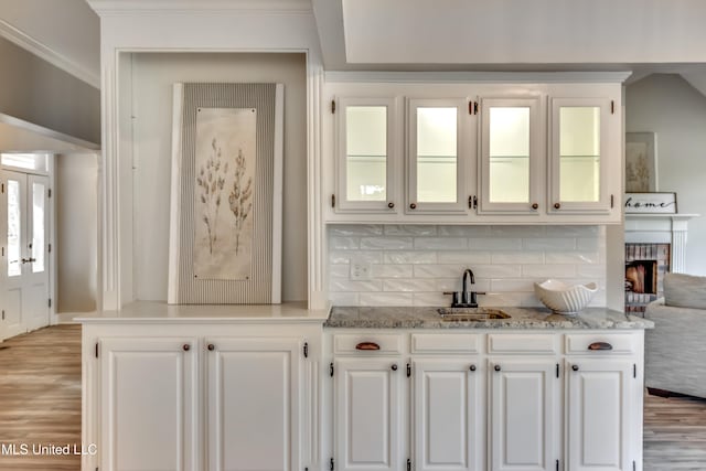 bar featuring white cabinetry, sink, light stone counters, a fireplace, and light wood-type flooring