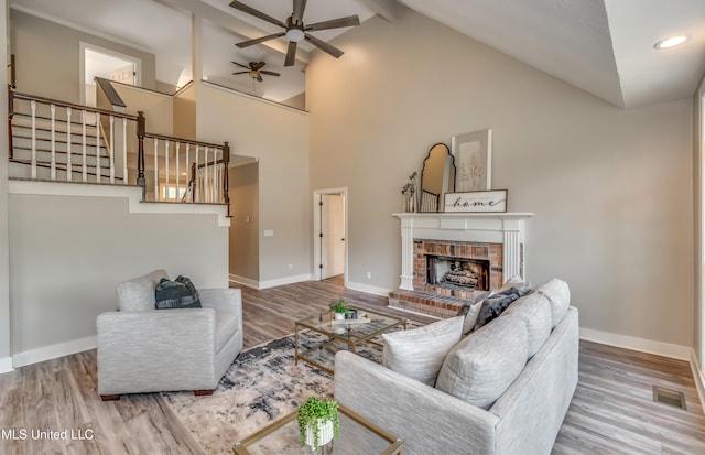 living room with wood-type flooring, beam ceiling, high vaulted ceiling, a brick fireplace, and ceiling fan