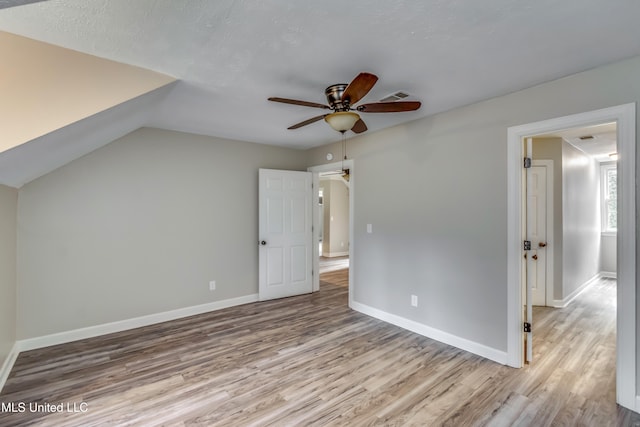 unfurnished bedroom featuring light wood-type flooring, lofted ceiling, a textured ceiling, and ceiling fan