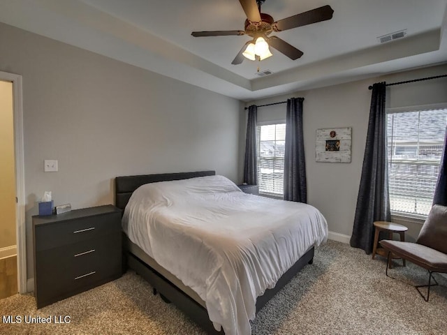 bedroom with light carpet, a tray ceiling, and ceiling fan