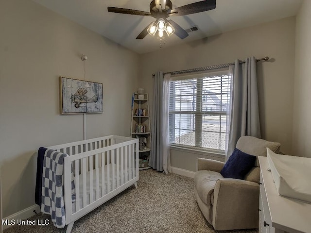 carpeted bedroom with ceiling fan and a crib