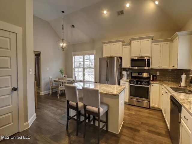 kitchen with pendant lighting, appliances with stainless steel finishes, a kitchen island, light stone counters, and white cabinetry