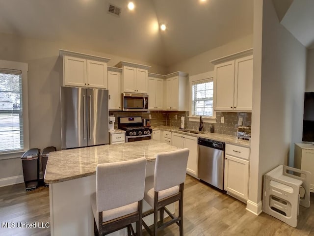 kitchen with a center island, light stone countertops, appliances with stainless steel finishes, and light hardwood / wood-style flooring