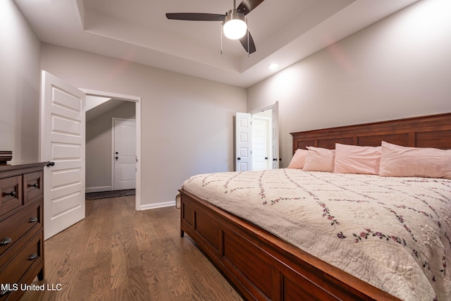 bedroom featuring ceiling fan, dark hardwood / wood-style flooring, and a tray ceiling