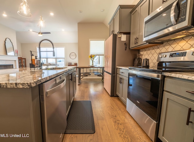 kitchen with decorative light fixtures, light hardwood / wood-style floors, tasteful backsplash, appliances with stainless steel finishes, and sink