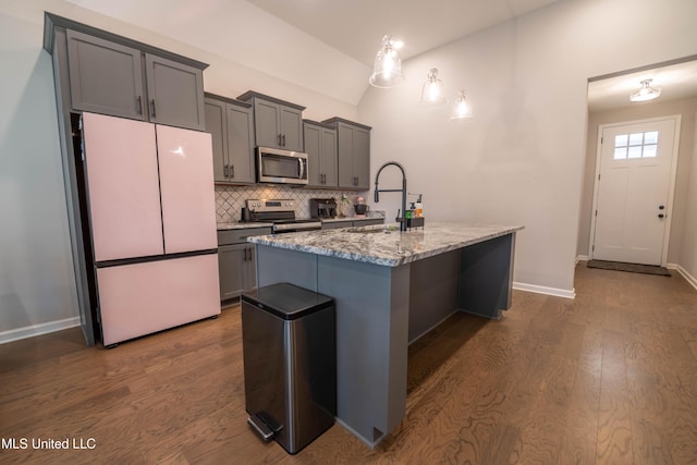 kitchen with light stone counters, stainless steel appliances, an island with sink, decorative backsplash, and sink