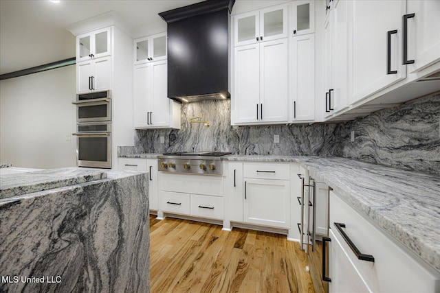 kitchen featuring decorative backsplash, custom exhaust hood, light wood-type flooring, white cabinetry, and appliances with stainless steel finishes