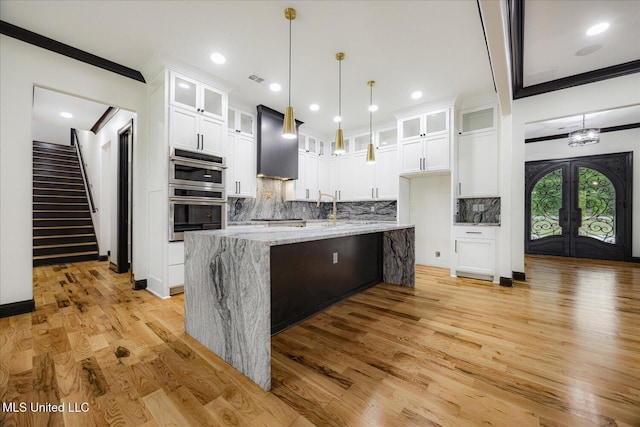 kitchen featuring wall chimney range hood, light wood-type flooring, backsplash, and stainless steel double oven