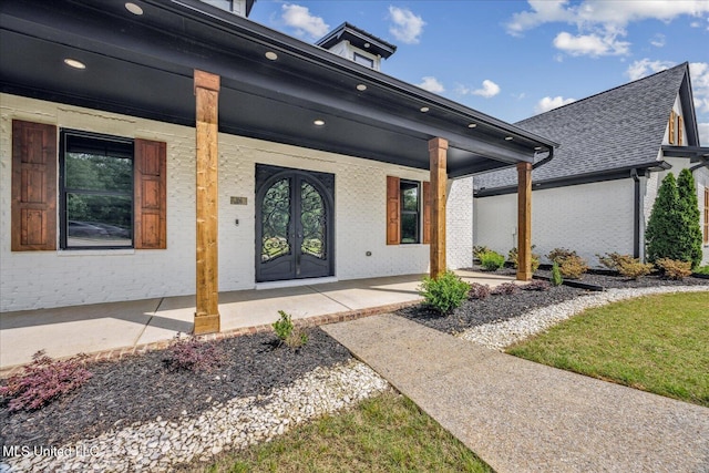 doorway to property featuring roof with shingles, covered porch, and brick siding