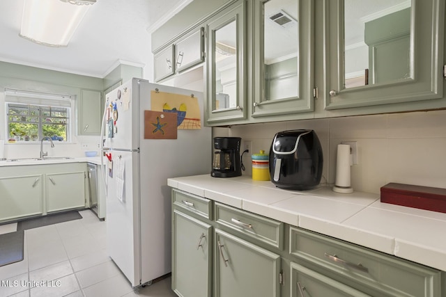kitchen featuring a sink, green cabinetry, freestanding refrigerator, and tasteful backsplash