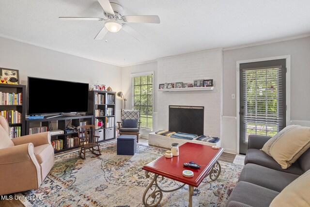 living area featuring ceiling fan, ornamental molding, a brick fireplace, and wood finished floors