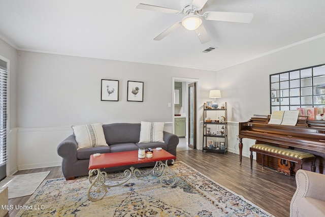 living room with ceiling fan, visible vents, wood finished floors, baseboards, and ornamental molding