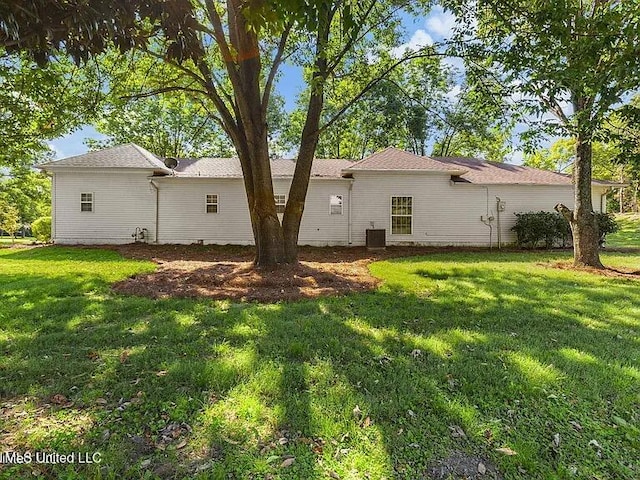 rear view of house with central AC and a lawn