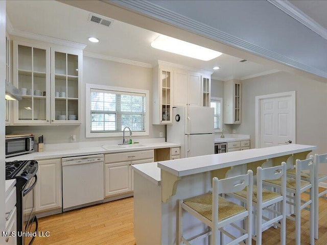 kitchen with white appliances, light wood-style flooring, visible vents, a breakfast bar, and a sink