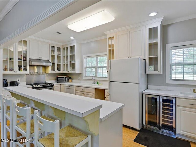 kitchen with ornamental molding, a kitchen breakfast bar, white appliances, under cabinet range hood, and beverage cooler