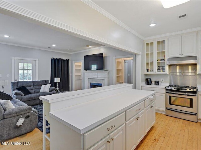 kitchen with ornamental molding, under cabinet range hood, gas stove, light countertops, and open floor plan