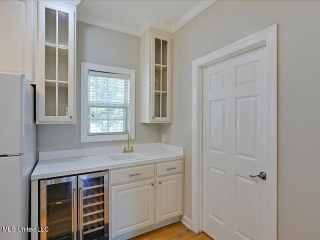 bar featuring freestanding refrigerator, light wood-style flooring, ornamental molding, a sink, and beverage cooler