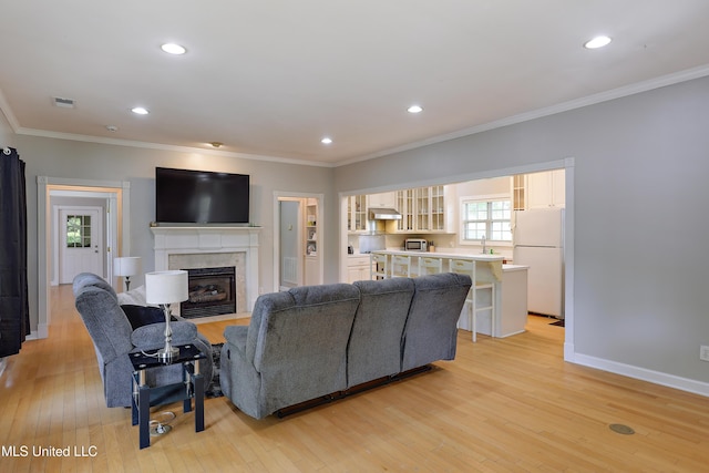 living area with light wood-style floors, a fireplace with flush hearth, visible vents, and ornamental molding