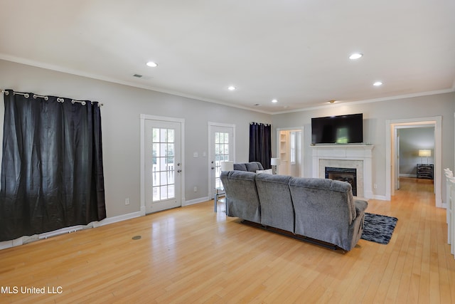 living area featuring light wood-style floors, ornamental molding, a glass covered fireplace, recessed lighting, and baseboards