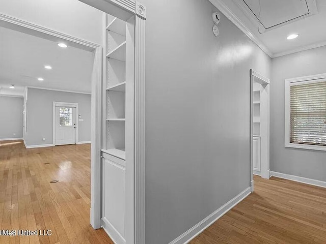 corridor with light wood-style floors, attic access, baseboards, and ornamental molding