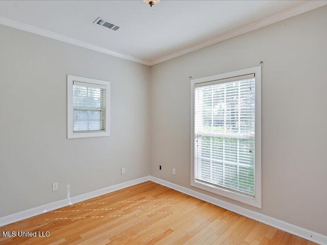 empty room featuring visible vents, baseboards, ornamental molding, and light wood-style flooring
