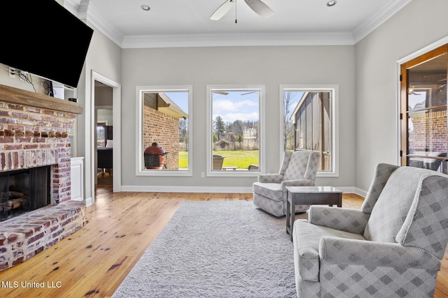 sitting room with ceiling fan, wood finished floors, baseboards, a brick fireplace, and crown molding